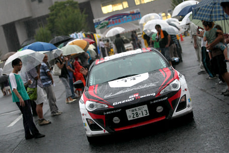 8月23日（金）、京都府京丹後市の京都府丹後文化会館で開催されたセレモニアルスタートはあいにくの雨模様。観客に手を振り、スタートしていくGAZOO Racingラック86。