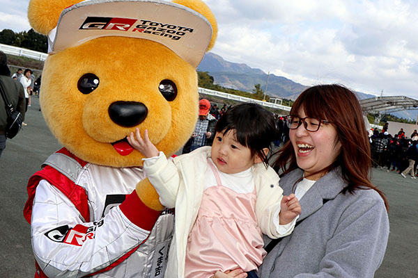 トヨタ くま吉 くま吉の口元に手を持ってく女の子を抱き上げてる女性と一緒に@ モースポフェス in 九州